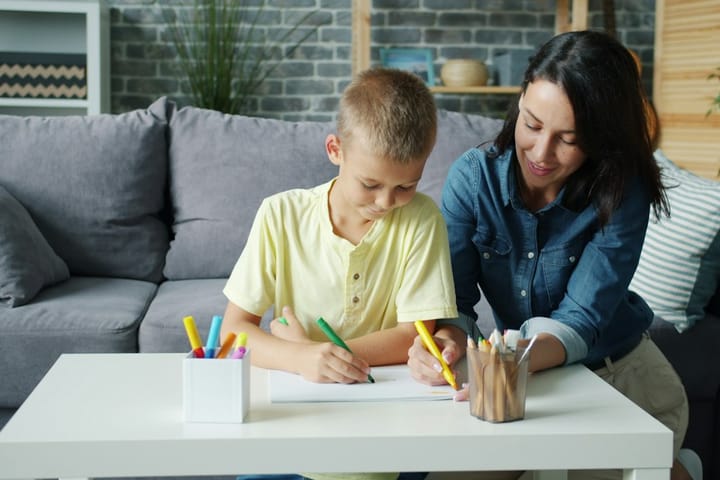 Menino desenhando à mesa acompanhado de uma profissional