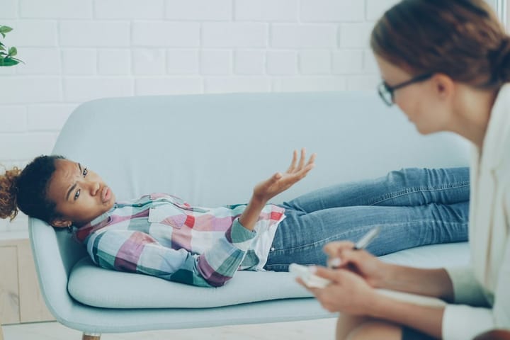 Terapeuta conversando com uma menina sentada no sofá do consultório